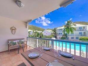 Ein Balkon mit Esstisch für vier Personen, einer Couch und Blick auf einen Pool sowie Gebäude.