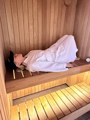 A sauna with a wooden bench and a person lying down.