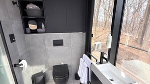 Et moderne badeværelse med et stort vindue, en hvid vask, et sort toilet og en håndklædestang.