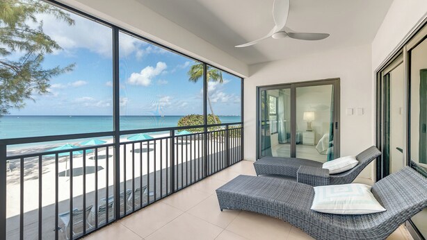 Un balcone con vista sull'oceano, una ventola a soffitto e due poltrone in vimini con cuscini.