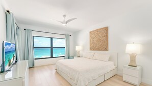 Una camera da letto con un letto grande, due comodini con lampade, una ventola a soffitto, un televisore su un mobile e una finestra vista oceano.