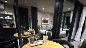 A modern hotel room with a round wooden table, black chairs, a sofa, and a bed. - Luxury Mirror Cabin with Lake View - Nature (Mountainburg)