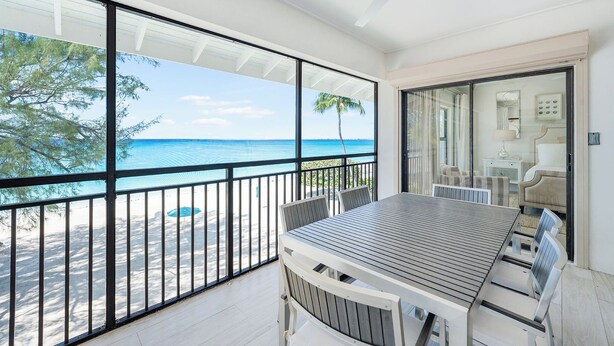 Ein Balkon mit Blick auf Strand und Meer, ein Tisch mit Stühlen und ein Deckenventilator.
