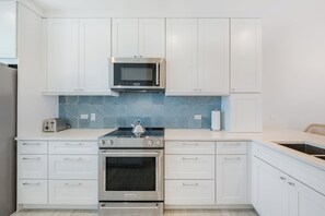 A modern kitchen with white cabinetry, a built-in microwave, a gas stove, and a stainless steel oven. - Casa Caribe #23 - 3 Bed, 2 Bath - Oceanfront, Third Floor (Seven Mile Beach)