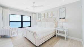 Ein modernes Schlafzimmer mit einem großen Bett, einem Nachttisch, einem Sessel und Meerblick.