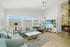A living room with a sofa, coffee table, TV, fireplace, and stone wall. - Family Beach Retreat | Heated Pool | Sleeps 8 | Near Beach (Bonita Springs)