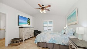 Un dormitorio con cama, ventilador de techo, televisión, cómoda, silla y ventana con persianas.