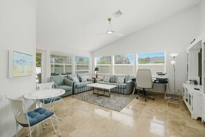 A living room with a sofa, coffee table, and chairs, a desk with a computer, and a window with blinds. - Family Beach Retreat | Heated Pool | Sleeps 8 | Near Beach (Bonita Springs)