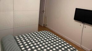 Een slaapkamer met een bed, een aan de muur bevestigde televisie en een kledingkast.