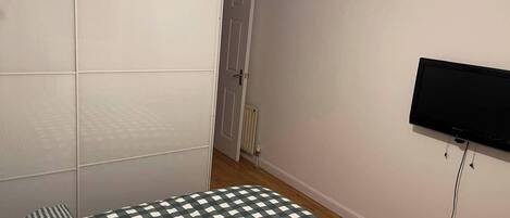 A bedroom with a bed, a television mounted on the wall, and a wardrobe.