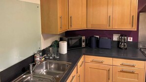 Een keuken met houten kastjes, een roestvrijstalen spoelbak, een magnetron, een waterkoker en een broodrooster.