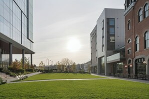 A modern building with a glass facade, a brick structure, and a green lawn area. - Hotel West & Main Conshohocken Philadelphia, Tapestry by Hilton (Conshohocken)