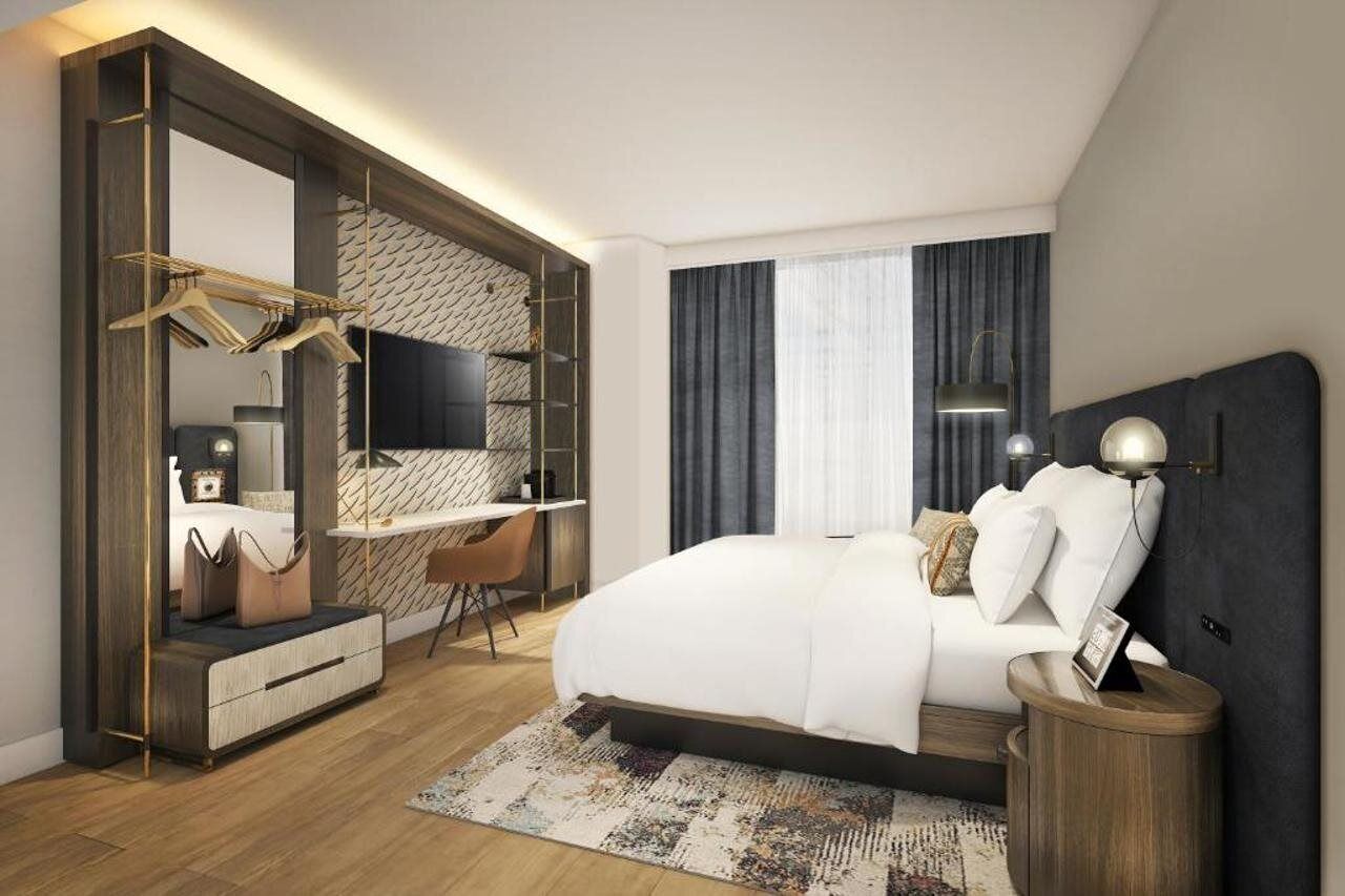A modern hotel room with a bed, desk, and wardrobe.