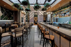 Zona de bar con asientos, barra, plantas colgantes y pared de ladrillo.