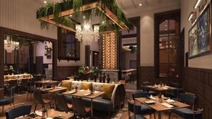 Un ristorante con tavoli in legno, sedie imbottite blu, una zona salotto centrale con una panca e un lampadario.