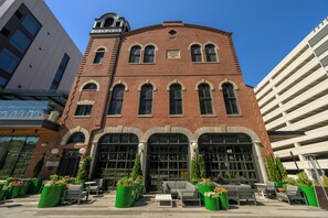 A historic brick building with large arched windows and a clock tower, surrounded by outdoor seating and greenery. - Hotel West & Main Conshohocken Philadelphia, Tapestry by Hilton (Conshohocken)