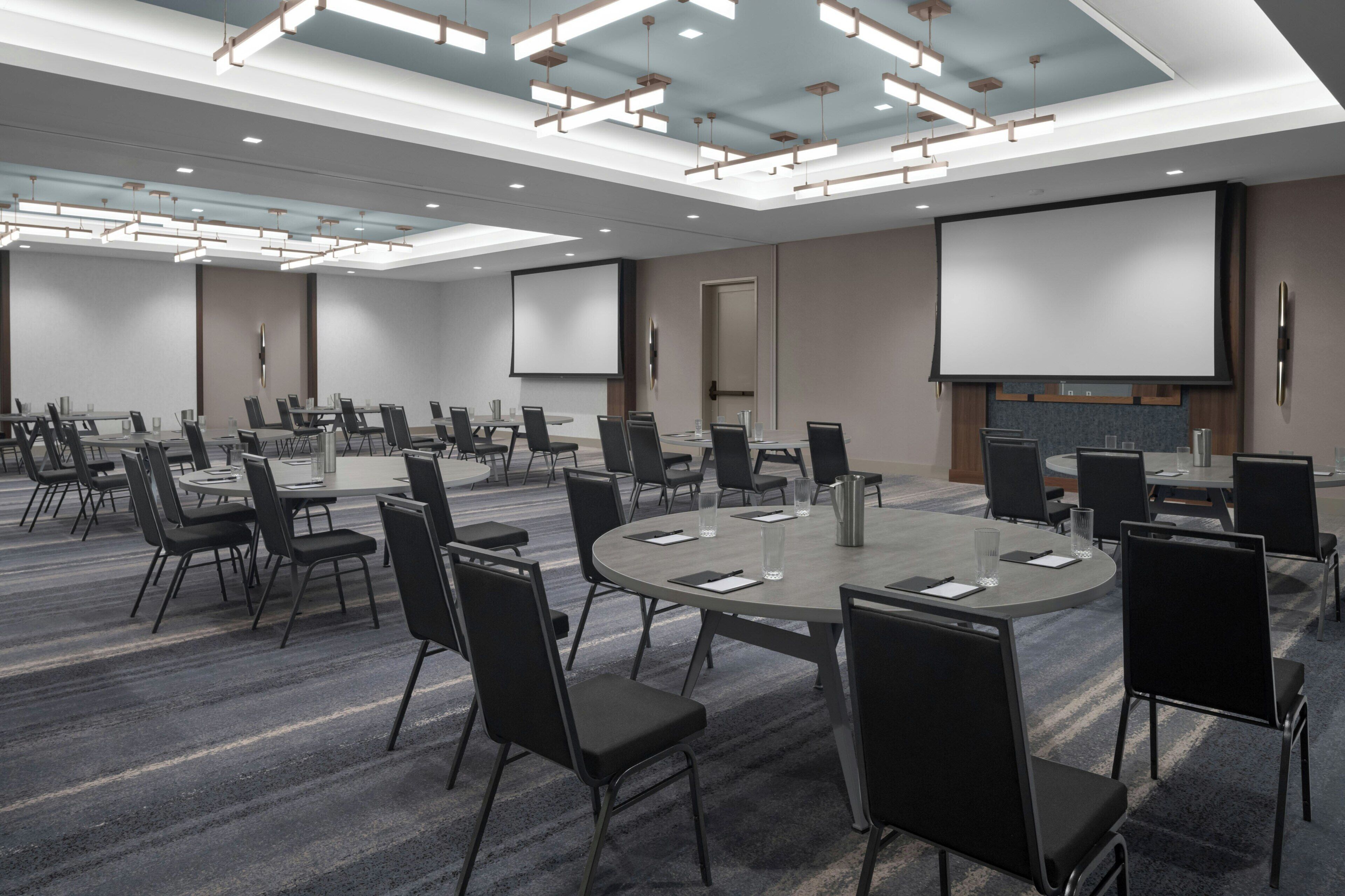 A conference room with multiple tables and chairs, a large screen, and a fireplace.