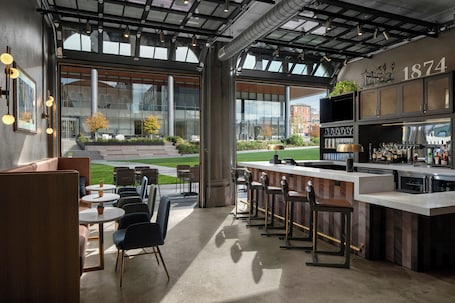 A modern bar area with a counter, stools, and a large window offering a view of the outdoors.. Hotel West & Main Conshohocken Philadelphia, Tapestry by Hilton