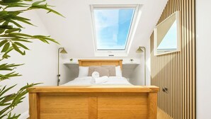 Un dormitorio con tragaluz, cama de madera, lámparas de noche y vistas al cielo.