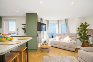 Ein modernes Wohnzimmer mit einer Couch, einem Essbereich mit Tisch und Stühlen, einer Küche und Meerblick.