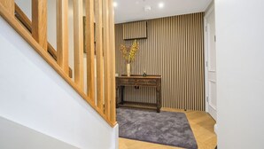 Una escalera con barandas de madera, una consola con un jarrón y un pared a rayas.