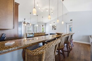 A kitchen with a long island counter, pendant lighting, and wicker bar stools.