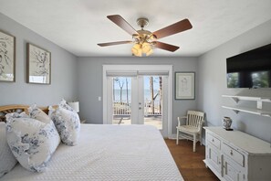 A bedroom with a bed, ceiling fan, artwork, and a view through a door.