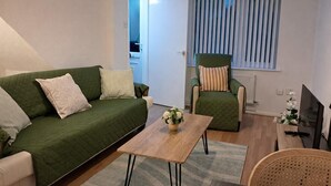 Ein Wohnzimmer mit einem grünen Sofa, einem Holztisch, einem grünen Sessel und einem Fenster mit Jalousien.