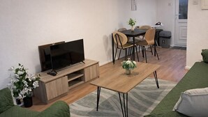 Ein Wohnzimmer mit Fernseher, Couch, Holztisch und einem Essbereich mit Stühlen und Tisch.