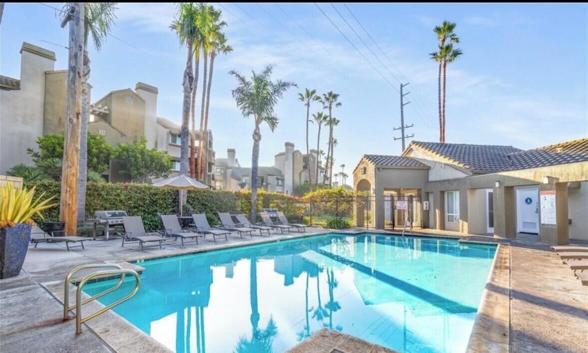 A swimming pool with lounge chairs, palm trees, and a building with a tiled roof.