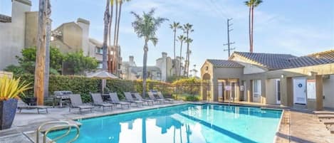 A swimming pool with lounge chairs, palm trees, and a building with a tiled roof.