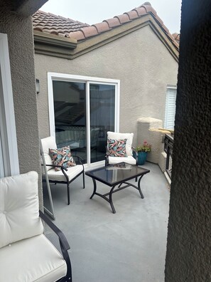 Ein Balkon mit Glastür, zwei weißen Sitzgelegenheiten mit Kissen, einem Glastisch und einem Blumentopf.