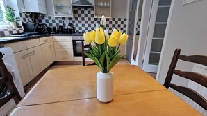 A kitchen with a checkered backsplash, a white vase with yellow flowers on the table, and a wooden chair. - 2 Bed Home - Parking, Wifi, Smart Tv (Nottingham)