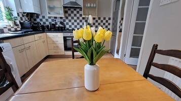 A kitchen with a checkered backsplash, a white vase with yellow flowers on the table, and a wooden chair.
