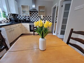 Eine Küche mit kariertem Fliesenspiegel, einer weißen Vase mit gelben Blumen auf dem Tisch und einem Holzhocker.