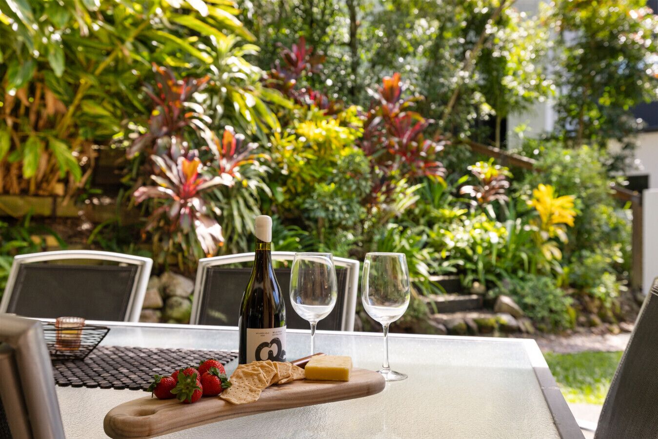 A table set outdoors with a bottle, glasses, strawberries, crackers, and cheese.