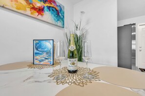 Una stanza con un tavolo in marmo, un cartello di benvenuto incorniciato, una bottiglia di champagne e due calici.