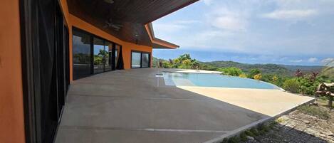 A modern house with a large pool, a covered patio, and a view of the surrounding landscape.