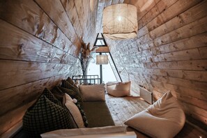 A cozy wooden interior with a sofa, pillows, and hanging lamps. - Family mountain retreat with jacuzzi, sauna, playground, and stunning forest views. (Sunger)