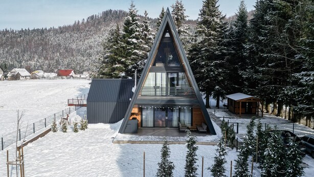 A modern, triangular-shaped building with large windows, surrounded by snow-covered trees and a clear sky. - Family mountain retreat with jacuzzi, sauna, playground, and stunning forest views. (Sunger)