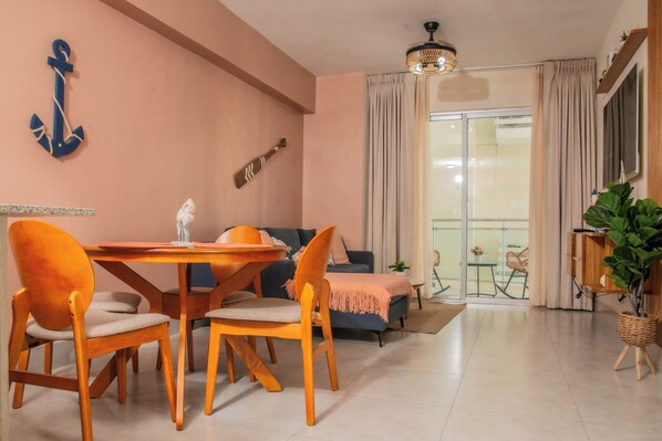 Un coin repas avec une table et des chaises en bois, un canapé et une vue sur l’extérieur grâce à une porte-fenêtre coulissante.