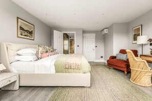 A bedroom with a bed, a red chair, a wicker chair, a lamp, and a painting on the wall. - The Luxury Boutique London Townhouse AC (London)
