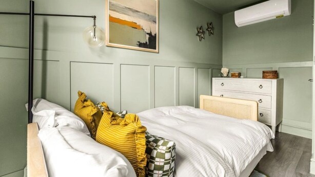 Ein Schlafzimmer mit Bett, Nachttisch, Schminktisch, Wand-Klimaanlage und einem Gemälde.