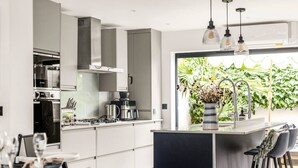 Eine moderne Küche mit Edelstahlgeräten, eine Essecke mit Barhocker und Blick ins Grüne.