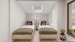 A narrow room with two beds, a skylight, a mirror, and a small plant. - The Luxury Secret Garden Retreat 3 bed 2 Bath (London)