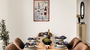A dining area with a round table, brown chairs, a hanging brass light fixture, and a framed artwork on the wall. - The Luxury Chic Duplex Apartment 2 Bed 2 Bath (London)