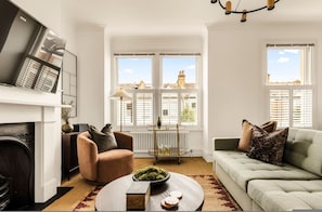 A living room with a fireplace, a sofa, a coffee table, and a view of buildings through large windows. - The Luxury Chic Duplex Apartment 2 Bed 2 Bath (London)