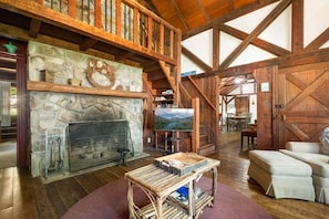 Un intérieur rustique agrémenté d’une cheminée en pierre, de poutres en bois, d’un coin repas et d’un espace salon confortable.