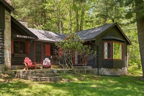 Eine rustikale Holzhütte mit Veranda, zwei Adirondack-Stühlen und einem kleinen Baum davor.