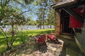 Un bâtiment en pierre avec une porte rouge, des sièges en plein air avec des fauteuils Adirondack, et une vue sur un lac.